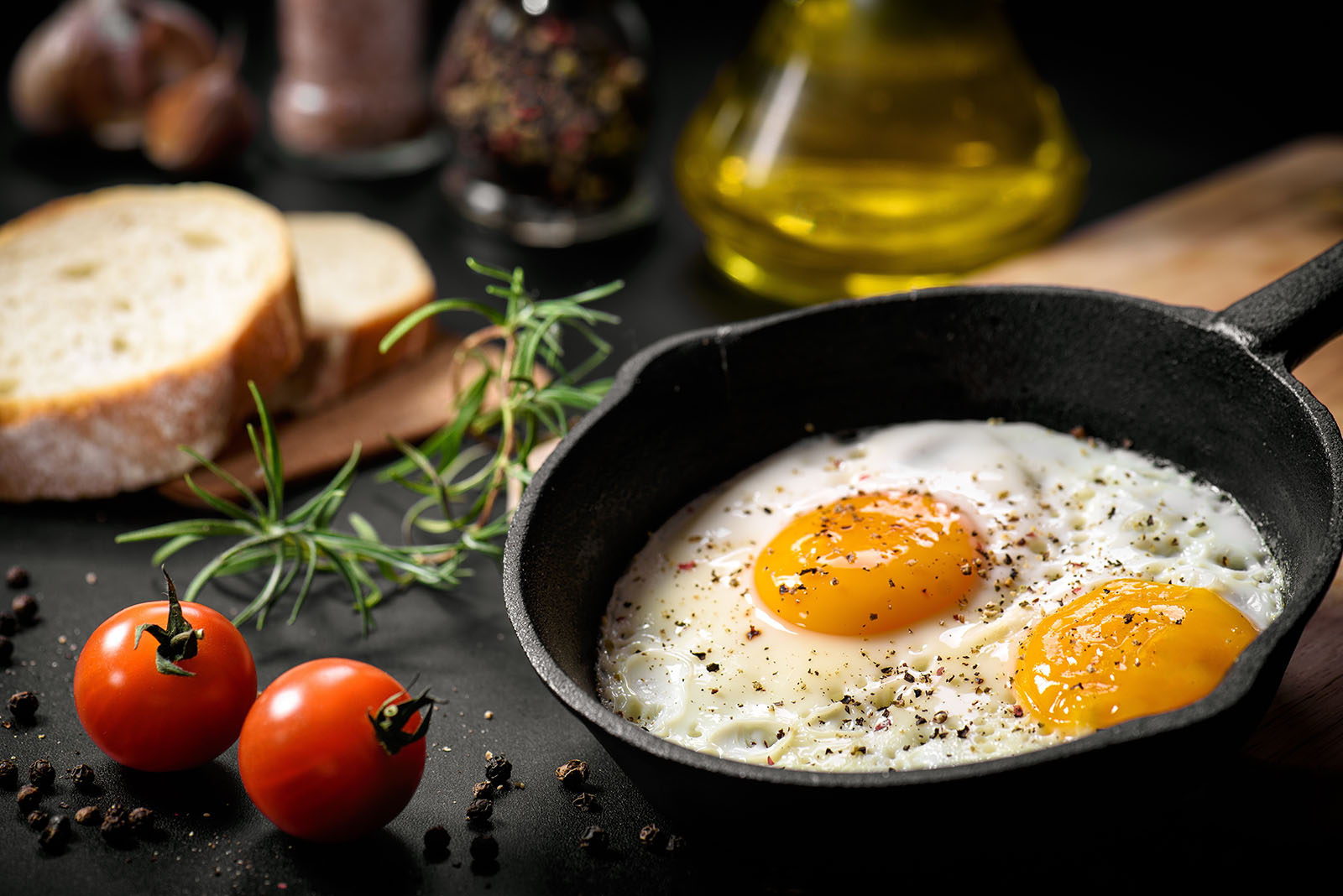 Fried egg cooked in a cast iron pan with tomatoes and olive oil to the side.